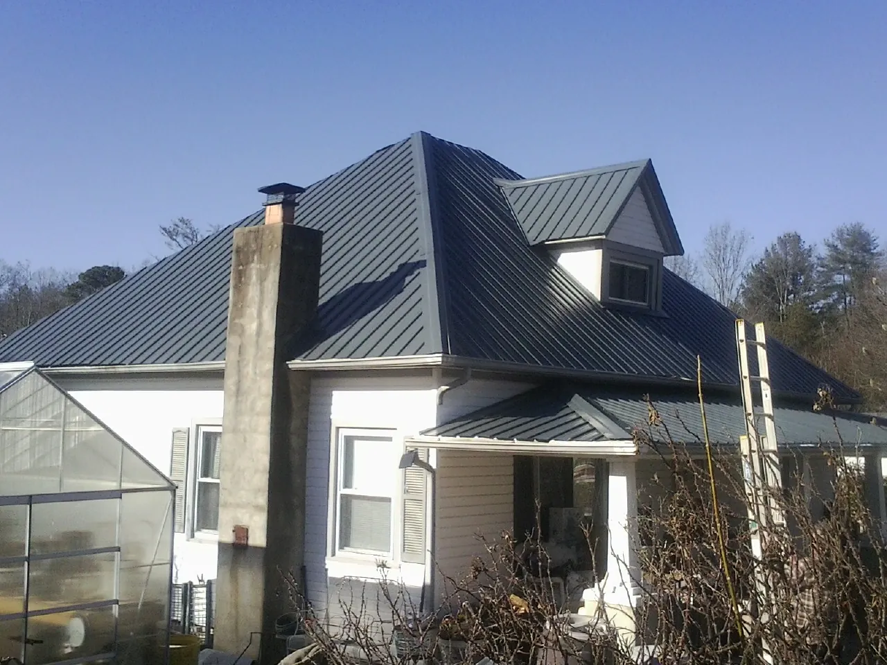 Dark blue standing seam metal roof on a white farmhouse with dormer — Slate & Tile Roof Repair by Roofing Brothers in Bristow