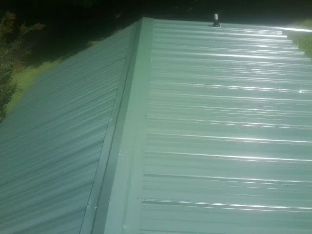 New green metal panels meeting at the ridge of a roof — Flat Roof Repair work by our crew in Bristow