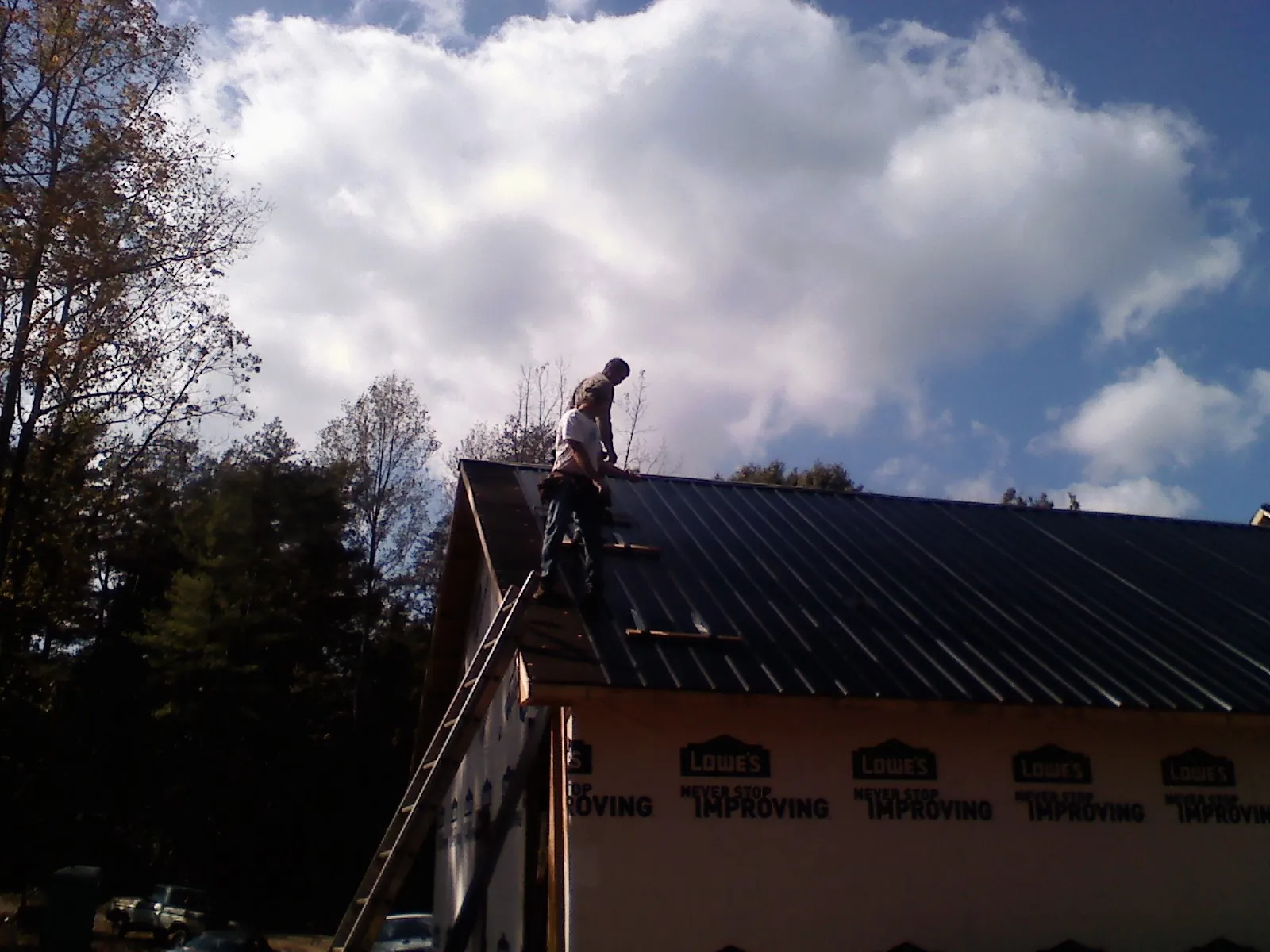 Roofer fastening dark metal panels high against a cloudy sky, from a Roof Inspection job in Bristow